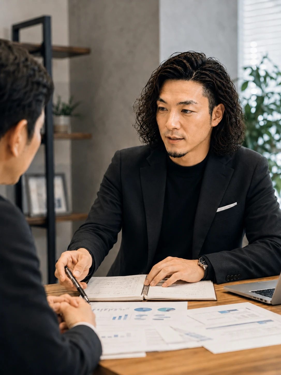 机をはさんで相談相手と向き合い、ノートを指しながら話す港秀樹（イメージ写真）